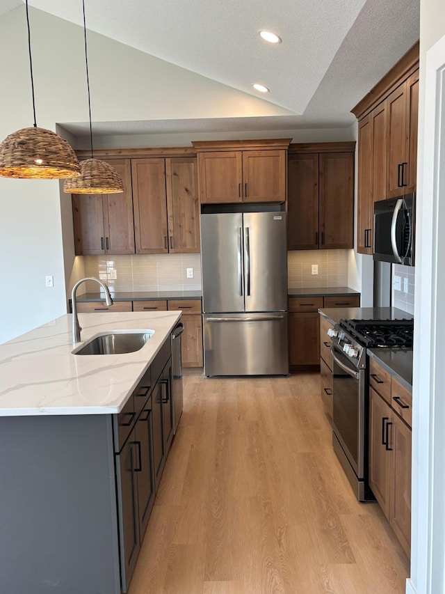 kitchen with lofted ceiling, a sink, decorative backsplash, light wood-style floors, and appliances with stainless steel finishes