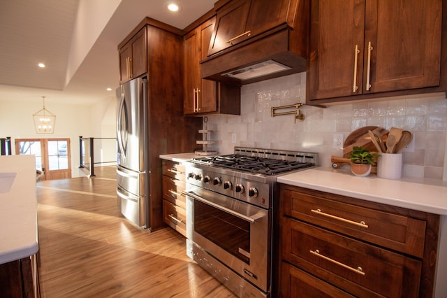 kitchen with premium range hood, decorative light fixtures, decorative backsplash, light hardwood / wood-style floors, and stainless steel appliances