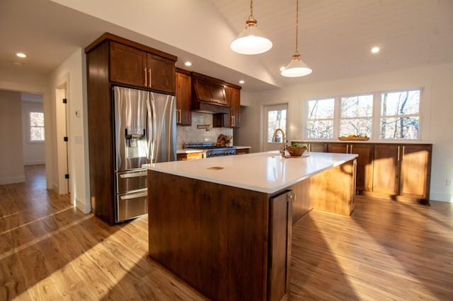 kitchen featuring lofted ceiling, an island with sink, decorative backsplash, stainless steel fridge with ice dispenser, and decorative light fixtures