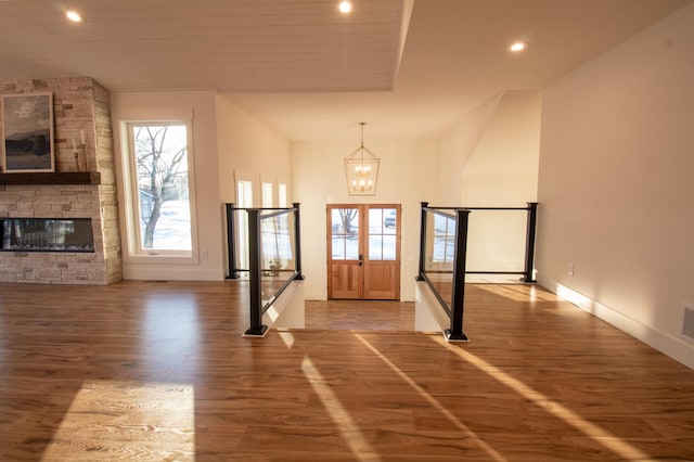 foyer entrance featuring a healthy amount of sunlight, wood-type flooring, a stone fireplace, and a notable chandelier