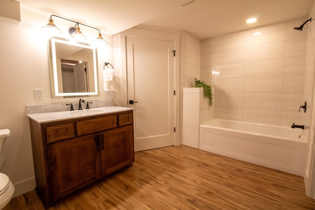 full bathroom with wood-type flooring, toilet, tiled shower / bath combo, and vanity