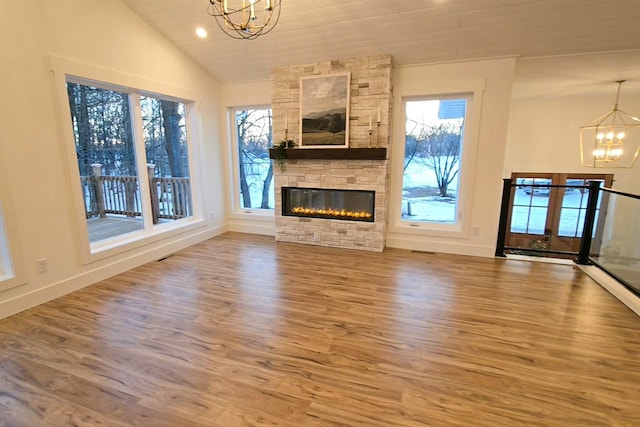 unfurnished living room featuring a healthy amount of sunlight, hardwood / wood-style floors, a stone fireplace, and a chandelier