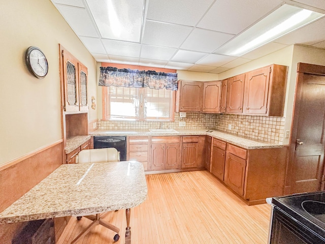 kitchen featuring a kitchen bar, a paneled ceiling, light wood-type flooring, decorative backsplash, and black appliances