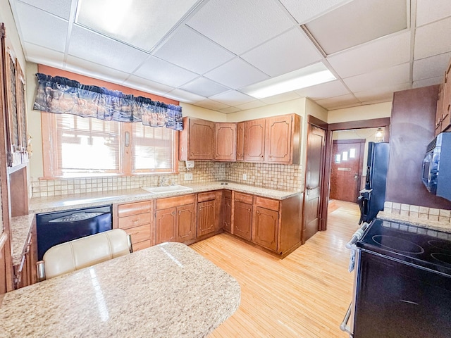 kitchen with a paneled ceiling, tasteful backsplash, sink, black appliances, and light wood-type flooring