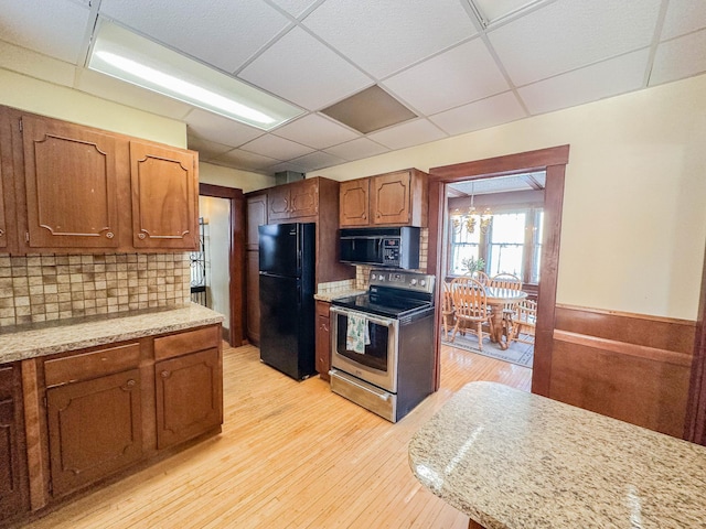 kitchen featuring light hardwood / wood-style flooring, tasteful backsplash, light stone countertops, black appliances, and a drop ceiling