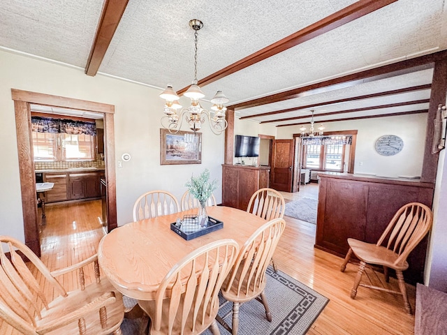 dining room featuring an inviting chandelier, a textured ceiling, light hardwood / wood-style floors, and beamed ceiling