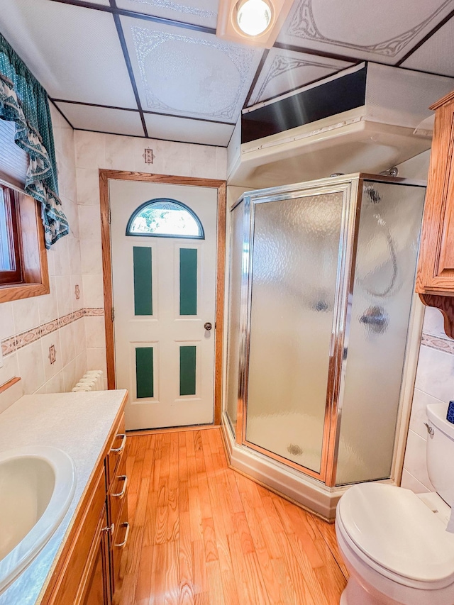 bathroom with tile walls, hardwood / wood-style flooring, vanity, toilet, and a shower with door