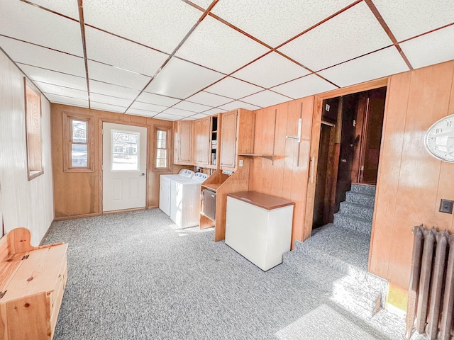 interior space featuring light colored carpet, wooden walls, radiator, and washer and dryer