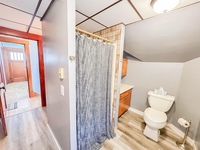 bathroom with hardwood / wood-style flooring, vanity, curtained shower, vaulted ceiling, and toilet