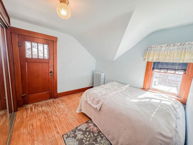 bedroom with hardwood / wood-style flooring, radiator, and vaulted ceiling