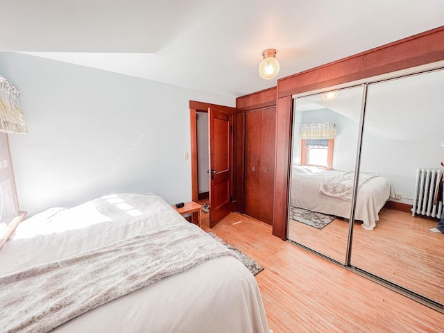 bedroom with light hardwood / wood-style flooring, radiator heating unit, lofted ceiling, and a closet