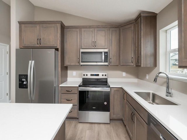 kitchen featuring vaulted ceiling, appliances with stainless steel finishes, sink, and light hardwood / wood-style floors