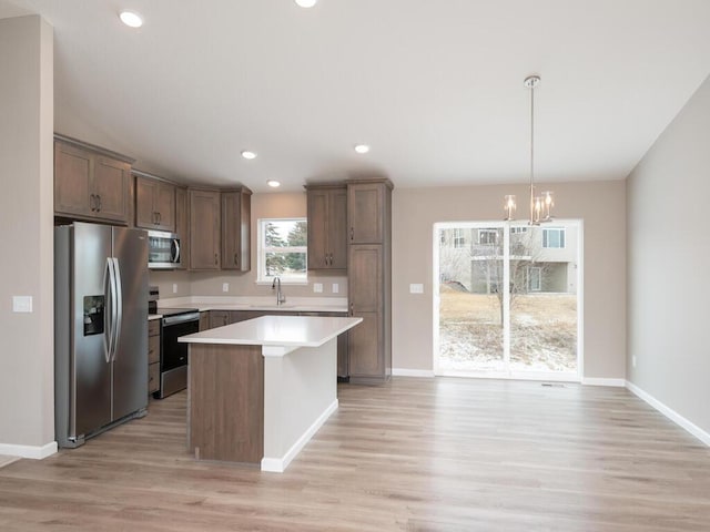 kitchen with appliances with stainless steel finishes, decorative light fixtures, sink, a center island, and light hardwood / wood-style floors