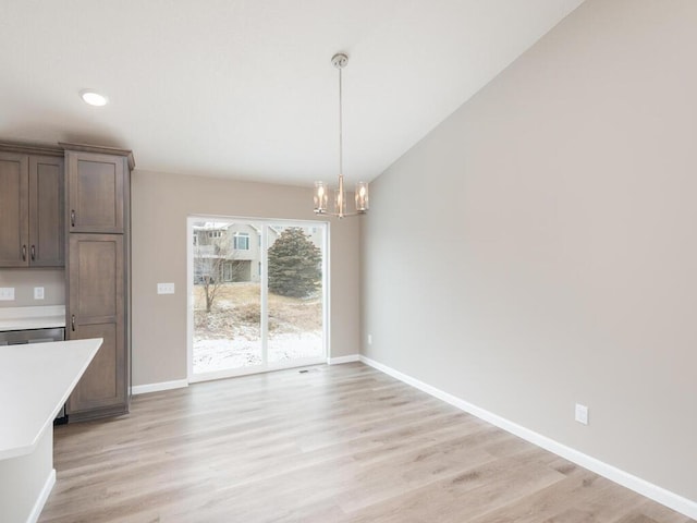 unfurnished dining area with an inviting chandelier, vaulted ceiling, and light hardwood / wood-style floors