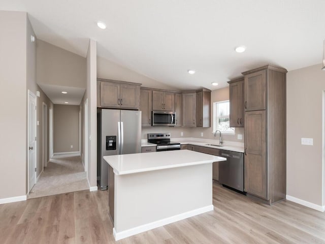 kitchen with sink, vaulted ceiling, appliances with stainless steel finishes, a kitchen island, and light hardwood / wood-style floors