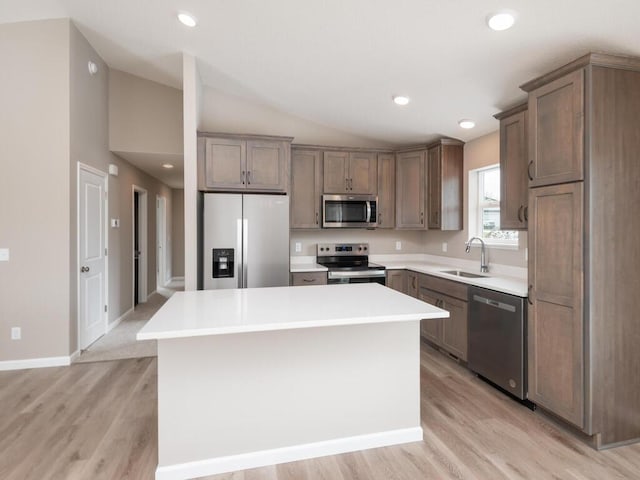 kitchen with a kitchen island, appliances with stainless steel finishes, lofted ceiling, sink, and light hardwood / wood-style floors