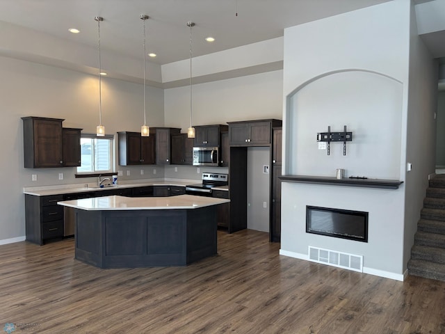 kitchen featuring dark brown cabinets, appliances with stainless steel finishes, dark hardwood / wood-style flooring, a kitchen island, and pendant lighting