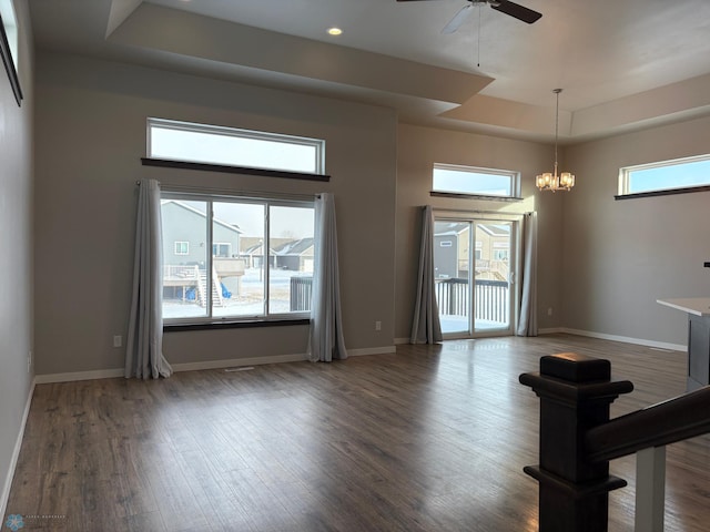 unfurnished living room featuring ceiling fan with notable chandelier, a towering ceiling, a raised ceiling, and hardwood / wood-style floors