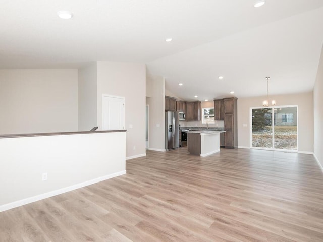 unfurnished living room featuring lofted ceiling, sink, a chandelier, and light hardwood / wood-style floors