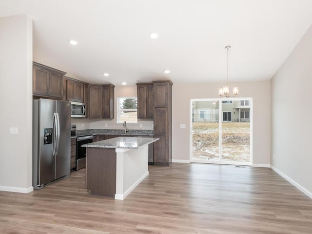 kitchen featuring pendant lighting, sink, a center island, stainless steel appliances, and light stone countertops