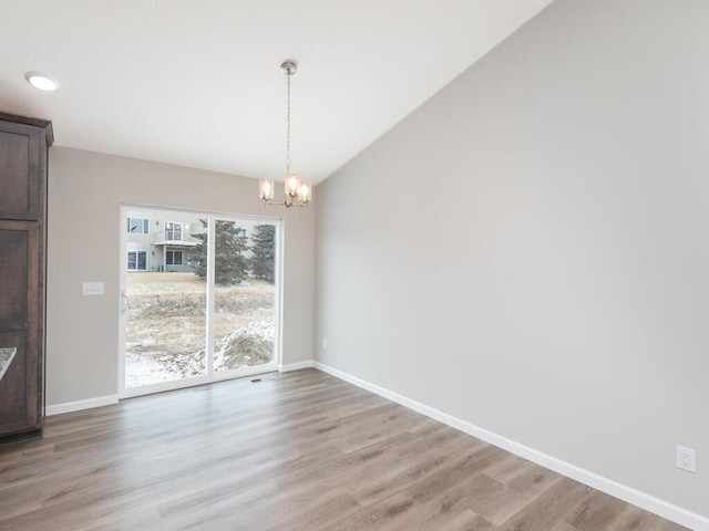 unfurnished dining area featuring lofted ceiling, an inviting chandelier, and light hardwood / wood-style flooring