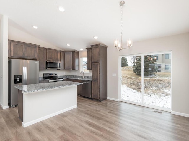 kitchen with appliances with stainless steel finishes, light stone countertops, a kitchen island, and plenty of natural light