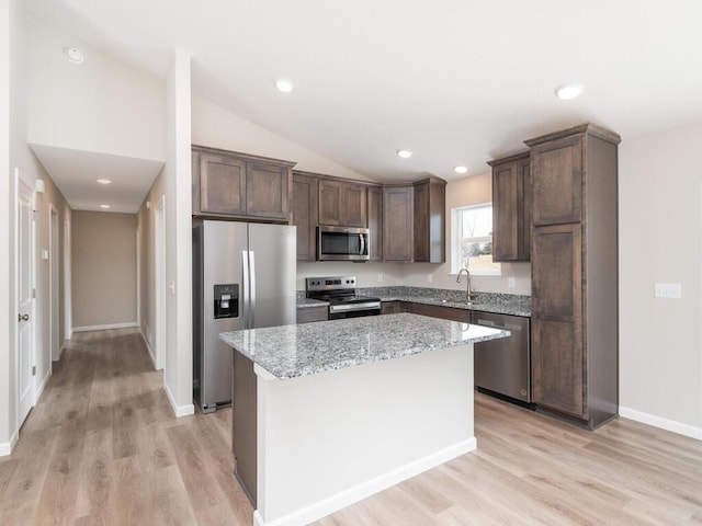 kitchen featuring vaulted ceiling, appliances with stainless steel finishes, a center island, light hardwood / wood-style floors, and light stone countertops