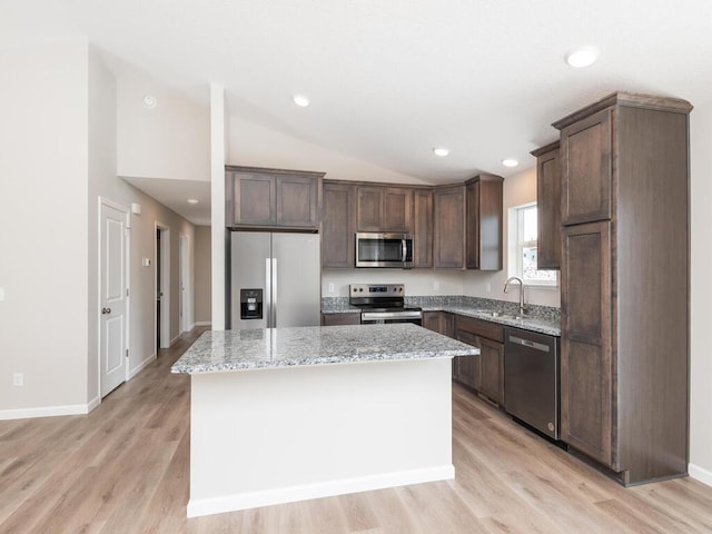 kitchen with sink, stainless steel appliances, a center island, light stone counters, and vaulted ceiling