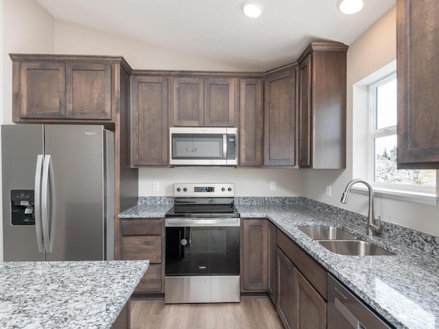 kitchen featuring vaulted ceiling, appliances with stainless steel finishes, sink, light stone countertops, and light wood-type flooring