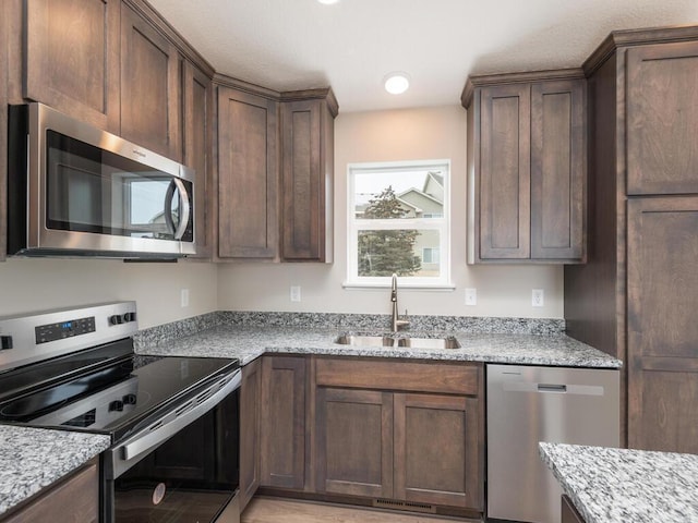 kitchen featuring light stone countertops, appliances with stainless steel finishes, sink, and dark brown cabinets