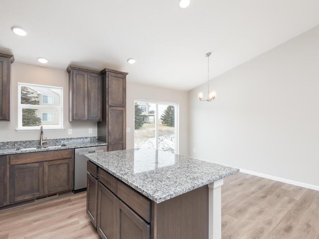 kitchen with a kitchen island, sink, hanging light fixtures, stainless steel dishwasher, and light stone counters