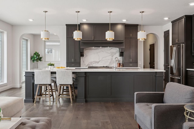 kitchen featuring hanging light fixtures, dark hardwood / wood-style floors, stainless steel fridge with ice dispenser, and a center island with sink