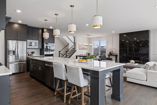 kitchen with dark wood-type flooring, hanging light fixtures, appliances with stainless steel finishes, a kitchen breakfast bar, and a kitchen island with sink