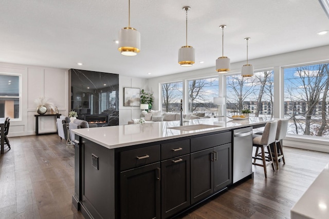 kitchen with hanging light fixtures, a premium fireplace, dark hardwood / wood-style floors, and a center island with sink