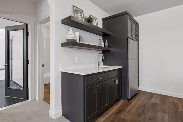 bar with dark hardwood / wood-style flooring, sink, stainless steel fridge, and dark brown cabinetry