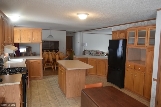 kitchen featuring stainless steel gas stove, sink, a center island, black fridge, and a textured ceiling