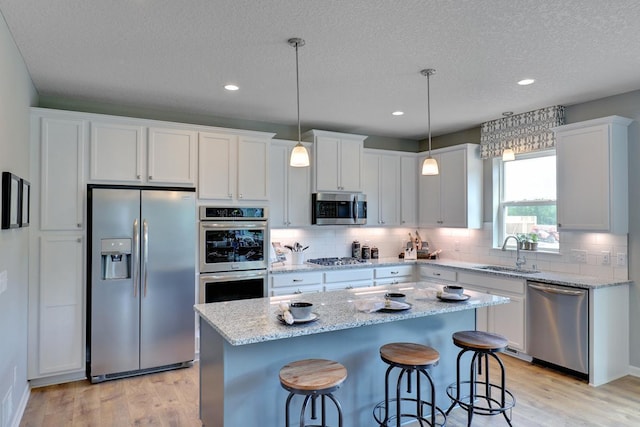 kitchen with sink, hanging light fixtures, a kitchen island, stainless steel appliances, and white cabinets