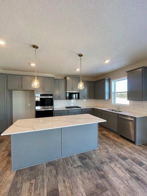 kitchen with stainless steel appliances, dark wood-style flooring, a center island, tasteful backsplash, and decorative light fixtures