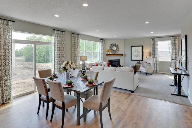 dining space featuring a textured ceiling, light wood-style flooring, recessed lighting, baseboards, and a glass covered fireplace