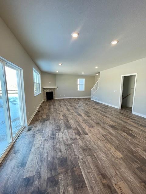 unfurnished living room featuring dark wood-style floors, a wealth of natural light, a fireplace, and baseboards