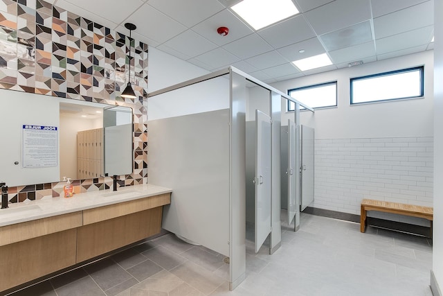 full bathroom featuring double vanity, a paneled ceiling, a stall shower, a sink, and tile patterned floors