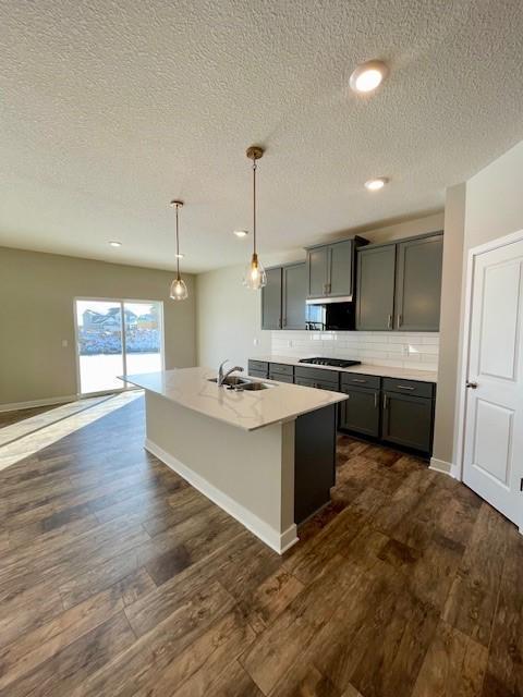 kitchen with gray cabinets, pendant lighting, an island with sink, sink, and dark wood-type flooring