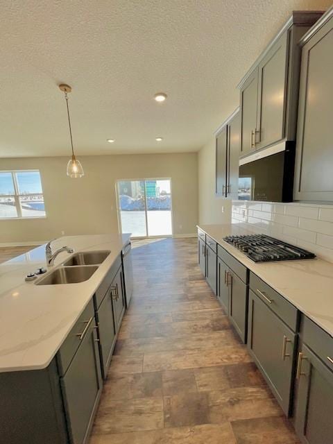 kitchen with sink, light stone counters, gas stovetop, decorative backsplash, and decorative light fixtures