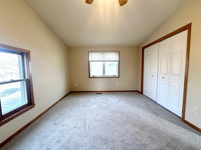 unfurnished bedroom featuring lofted ceiling, a closet, ceiling fan, and carpet