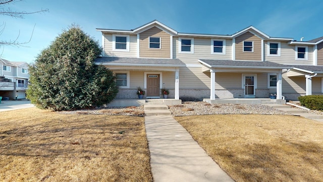 multi unit property with brick siding, a porch, and a front lawn