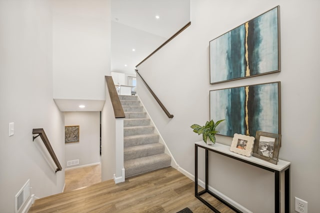 staircase with wood-type flooring and a high ceiling