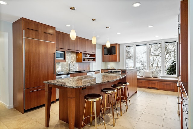 kitchen with pendant lighting, sink, dark stone countertops, backsplash, and built in appliances