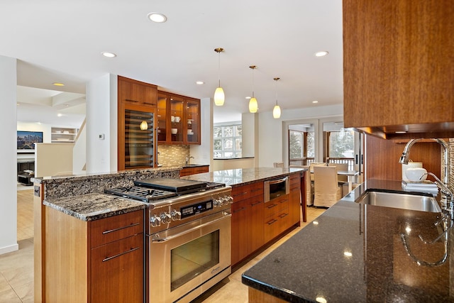 kitchen with high end stainless steel range, sink, hanging light fixtures, a kitchen island, and dark stone counters