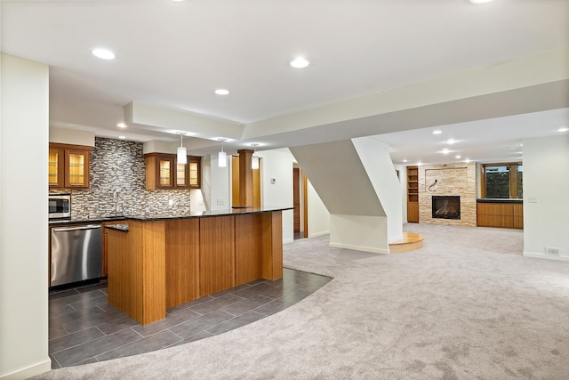 kitchen with hanging light fixtures, stainless steel appliances, a large fireplace, decorative backsplash, and dark carpet