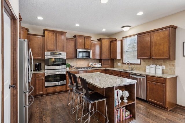 kitchen featuring dark hardwood / wood-style floors, a kitchen breakfast bar, a center island, stainless steel appliances, and light stone countertops